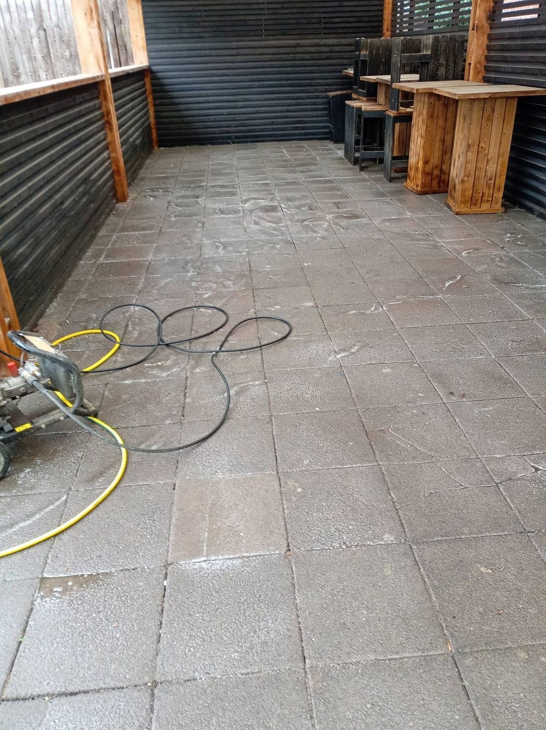 Patio being pressure washed, half cleaned with the jet washer visible